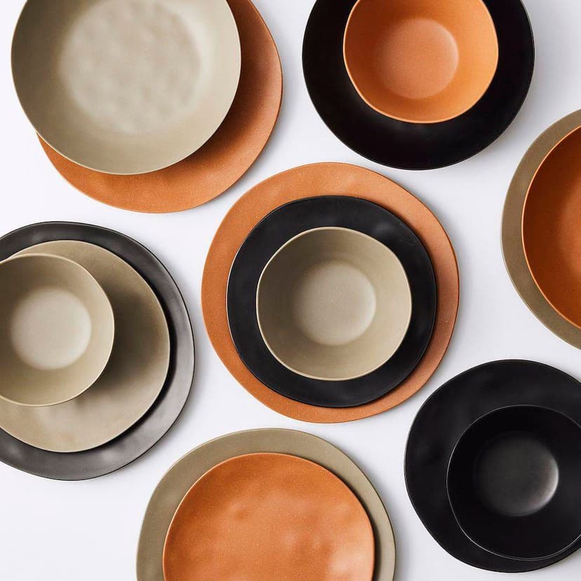 A pile of medium and large plates arranged in alternating patterns of gray, black, and brown colors on a white background.