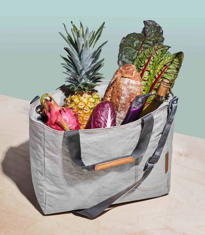 A gray cooler bag with vegetables, fruit, and a bottle of wine inside